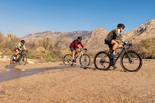 Three gravel cyclists riding through a river