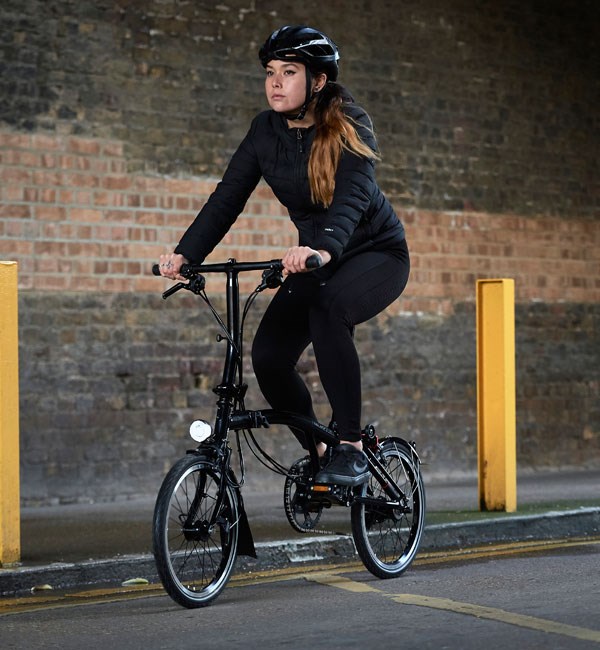 A cyclist riding a Brompton Black Edition folding bike through the streets