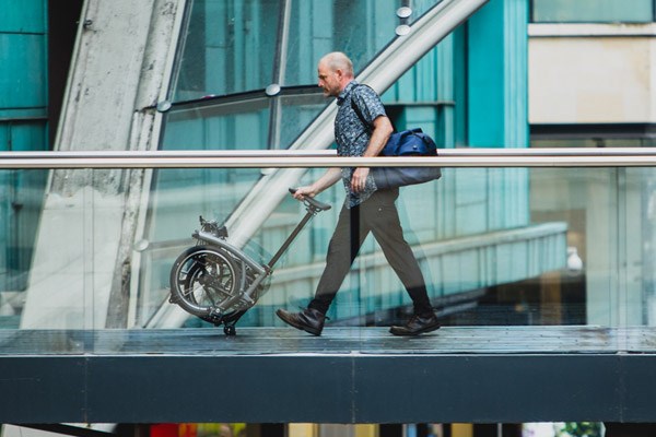 A cycle commuter pushes a folded Brompton through a shopping centre