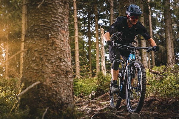 A mountain biker riding over a rocky & rooty trail